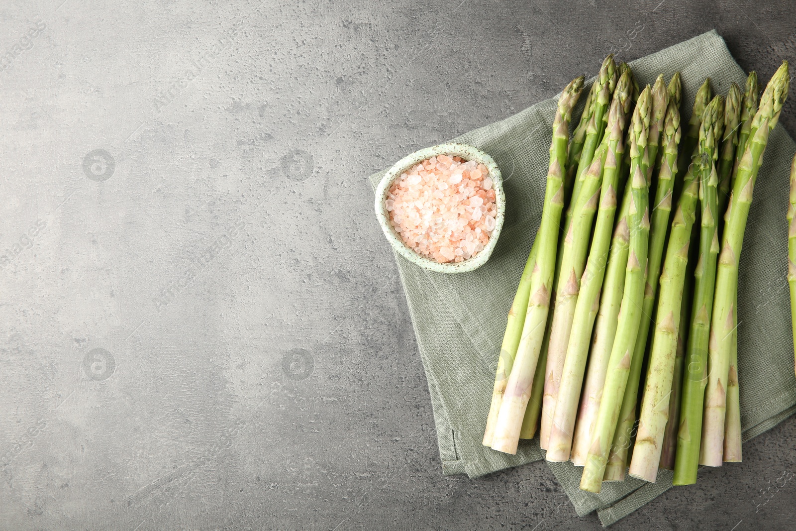 Photo of Fresh green asparagus stems and sea salt on grey textured table, top view. Space for text