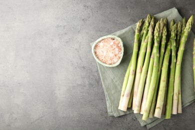 Fresh green asparagus stems and sea salt on grey textured table, top view. Space for text