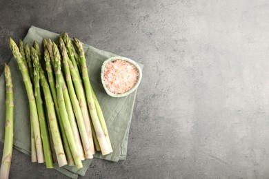 Photo of Fresh green asparagus stems and sea salt on grey textured table, top view. Space for text