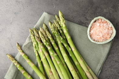 Photo of Fresh green asparagus stems and sea salt on grey textured table, top view