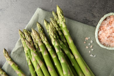 Photo of Fresh green asparagus stems and sea salt on grey textured table, top view