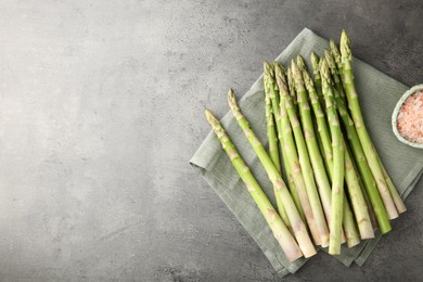 Photo of Fresh green asparagus stems and sea salt on grey textured table, top view. Space for text