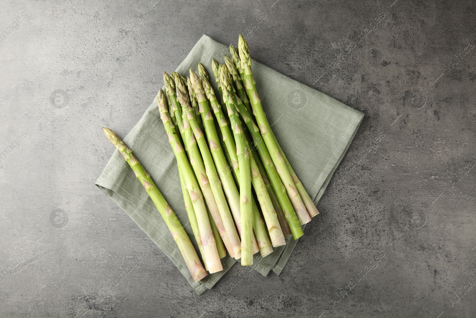 Photo of Fresh green asparagus stems on grey textured table, top view