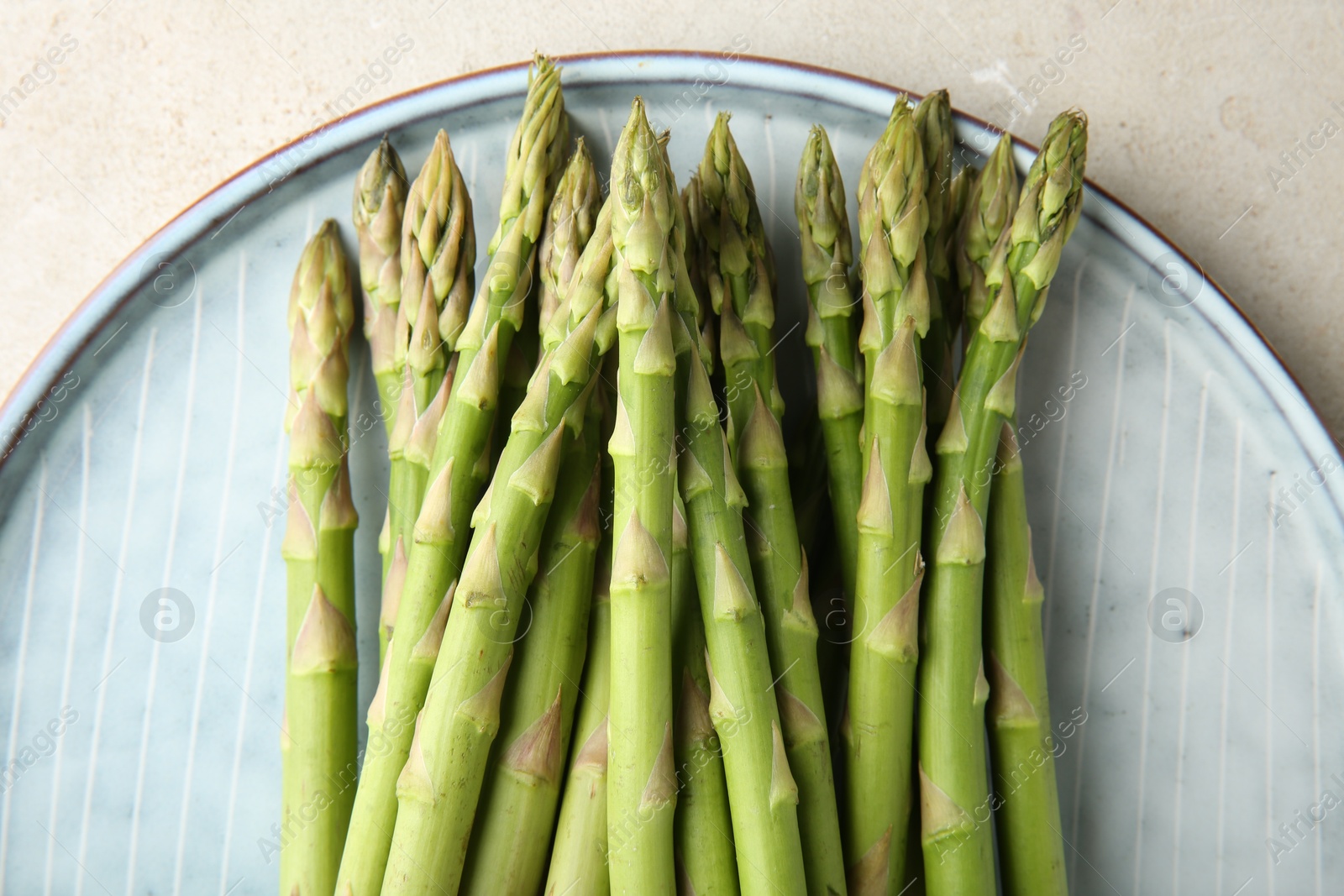 Photo of Plate with fresh green asparagus stems on light textured table, top view