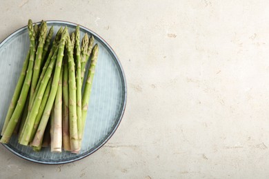 Photo of Plate with fresh green asparagus stems on light textured table, top view. Space for text