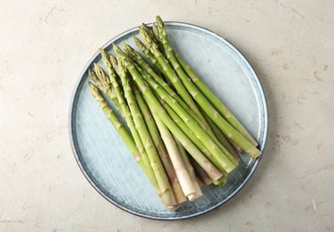 Photo of Plate with fresh green asparagus stems on light textured table, top view