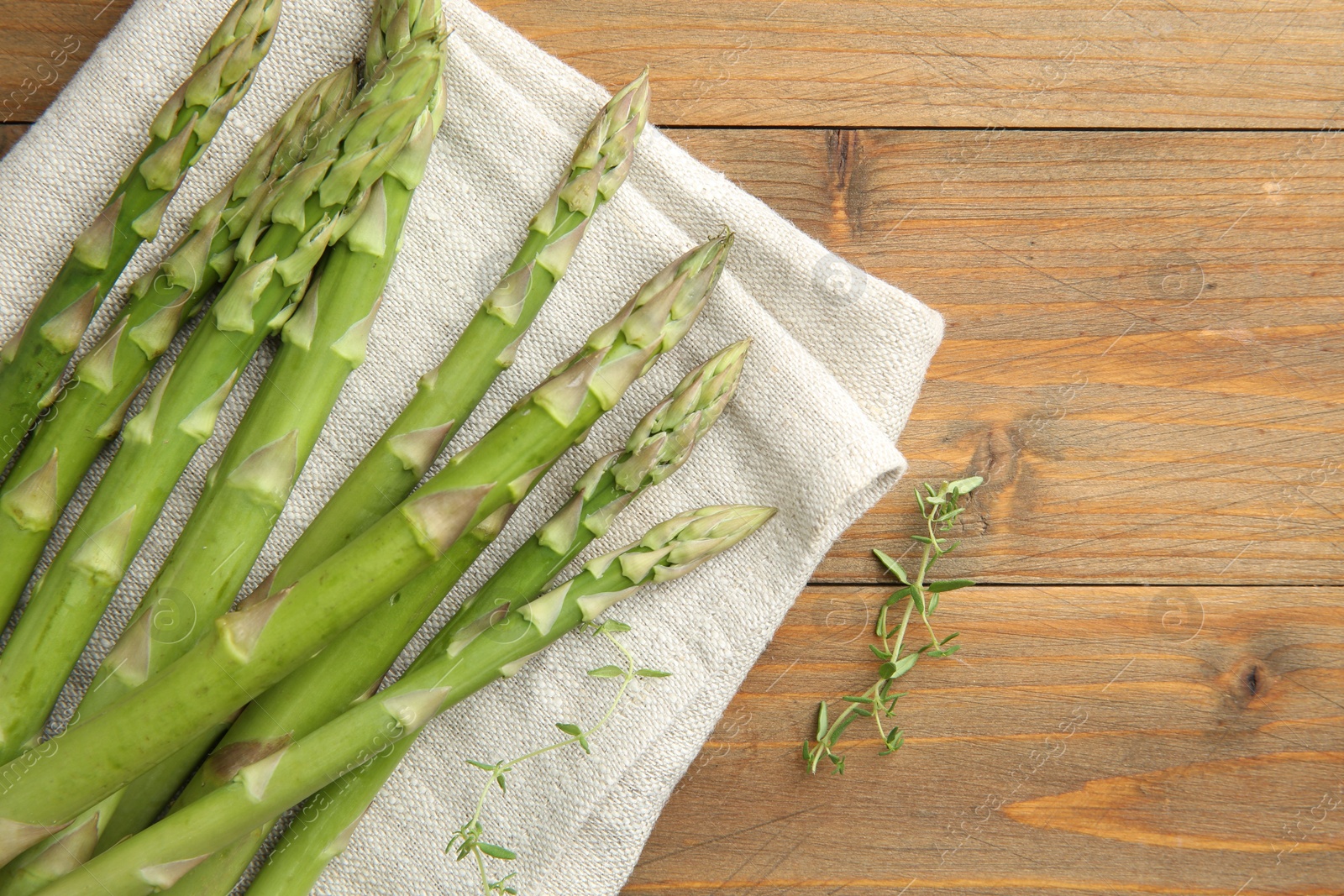 Photo of Fresh green asparagus stems and thyme on wooden table, top view