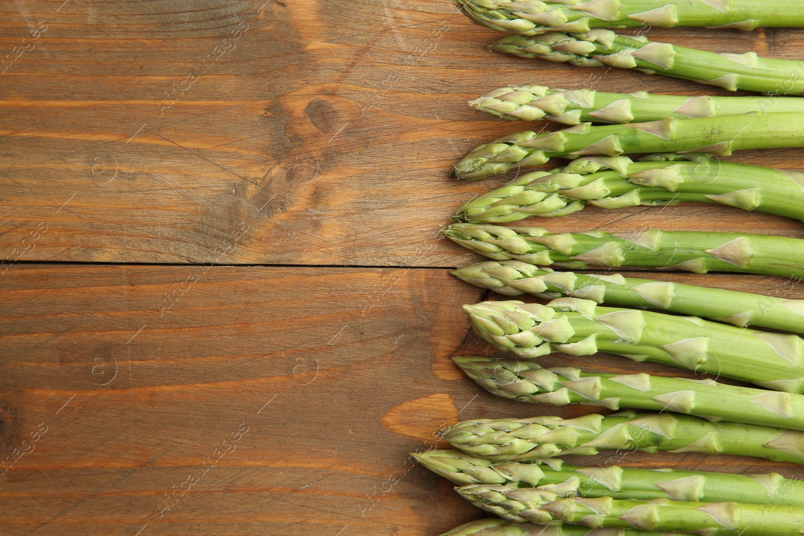 Photo of Fresh green asparagus stems on wooden table, top view. Space for text