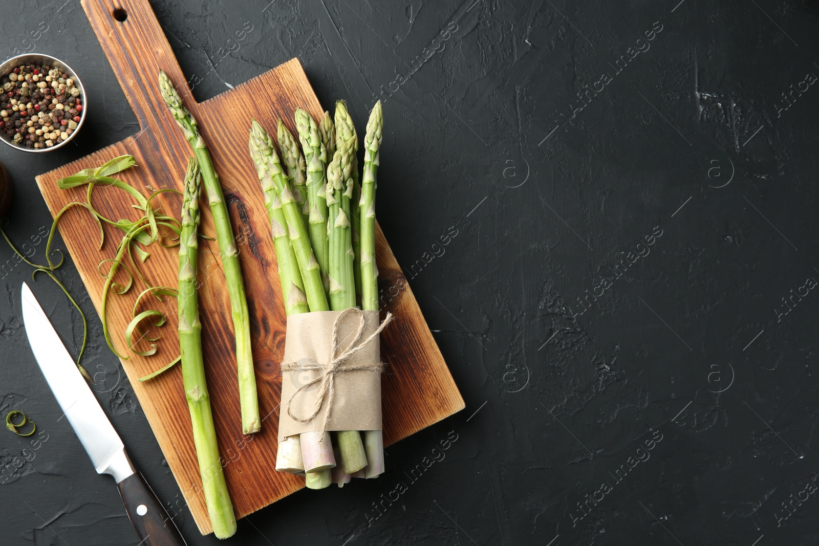 Photo of Fresh green asparagus stems, spices and knife on gray textured table, flat lay. Space for text