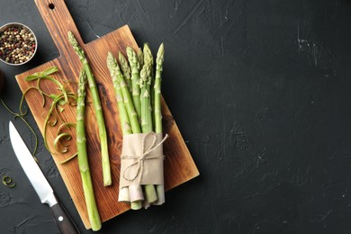 Photo of Fresh green asparagus stems, spices and knife on gray textured table, flat lay. Space for text