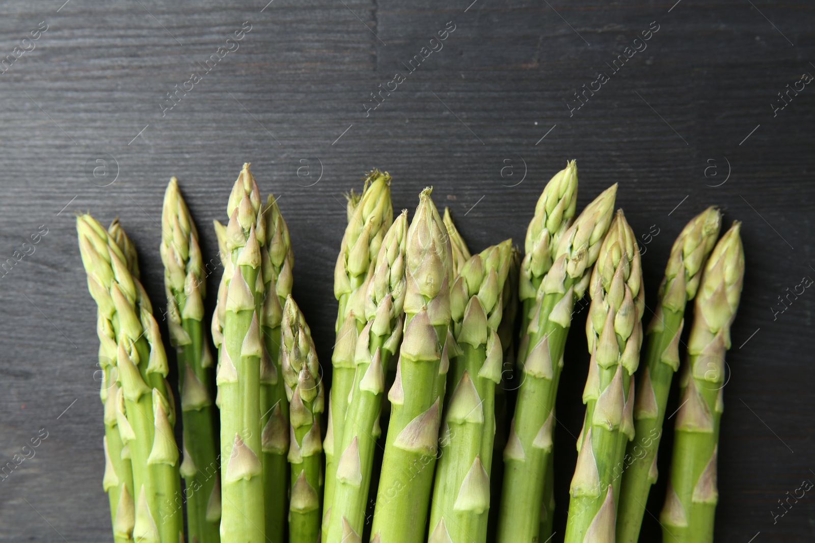 Photo of Fresh green asparagus stems on gray wooden table, top view