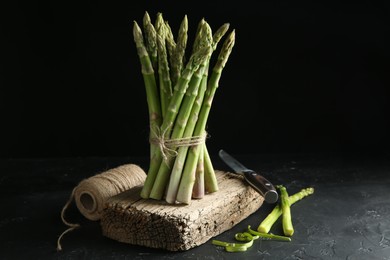 Photo of Fresh green asparagus stems, thread and knife on gray textured table against black background