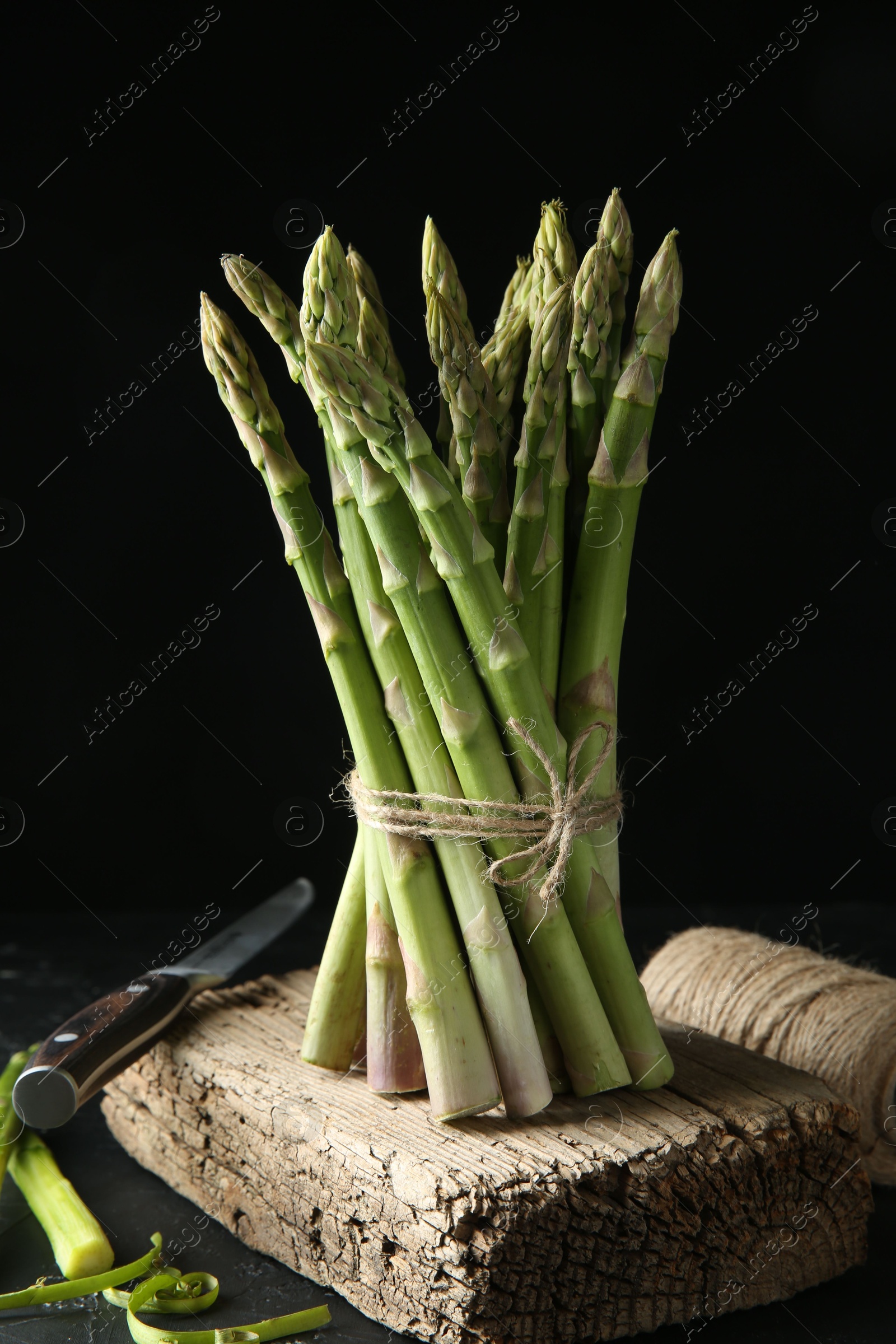 Photo of Fresh green asparagus stems, thread and knife on gray table against black background