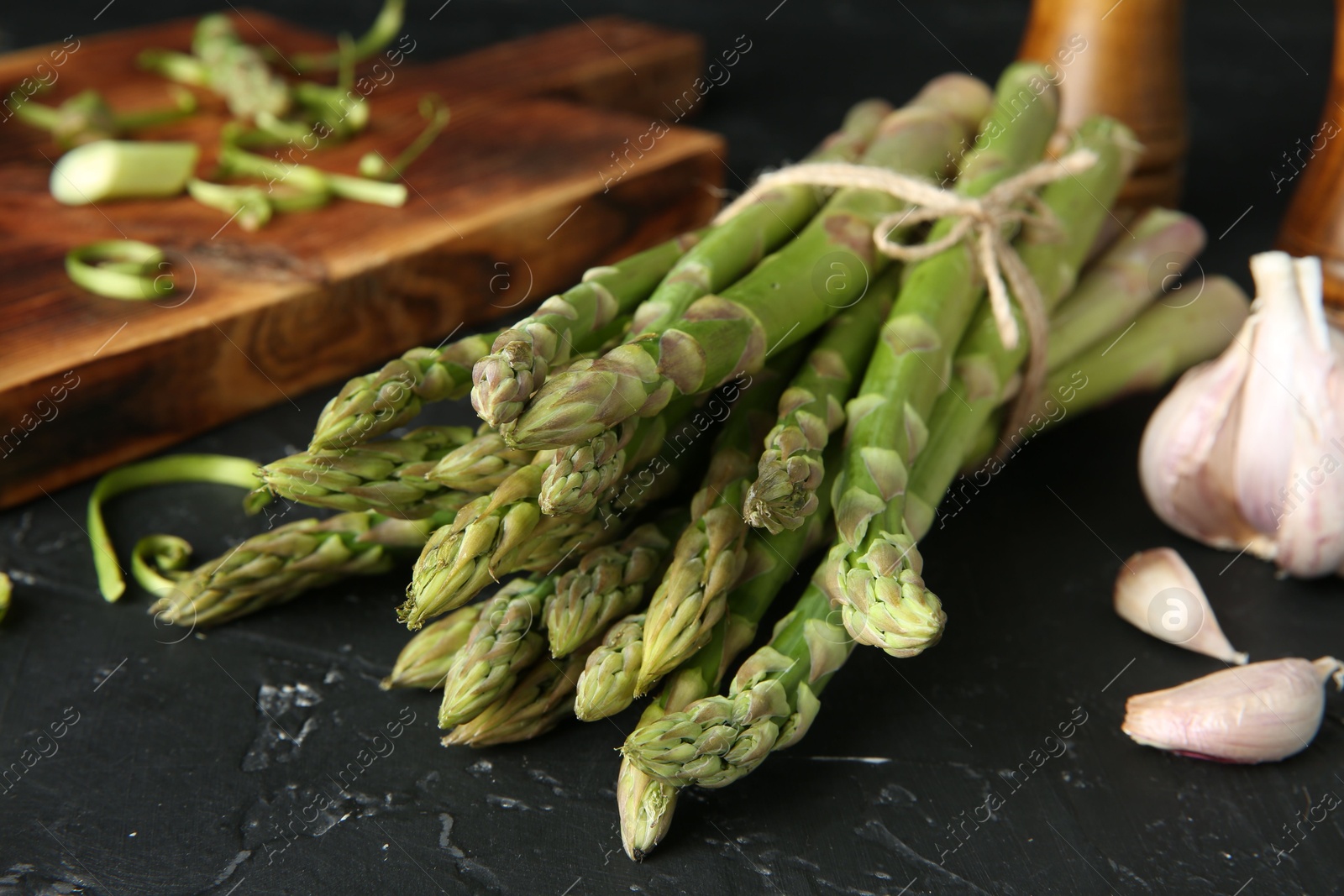 Photo of Fresh green asparagus stems and garlic on black textured table, closeup