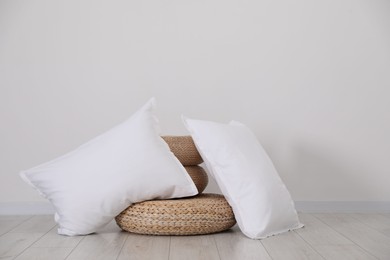 Clean pillows and wicker poufs on floor near white wall