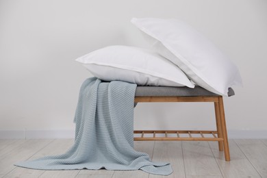 Clean pillows, blanket and storage bench on floor near white wall