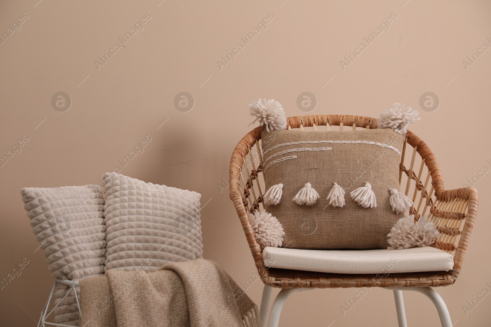 Photo of Soft pillows, wicker chair and blanket near beige wall