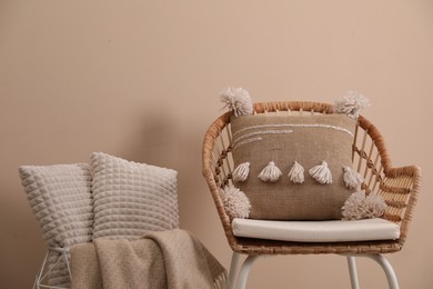 Soft pillows, wicker chair and blanket near beige wall