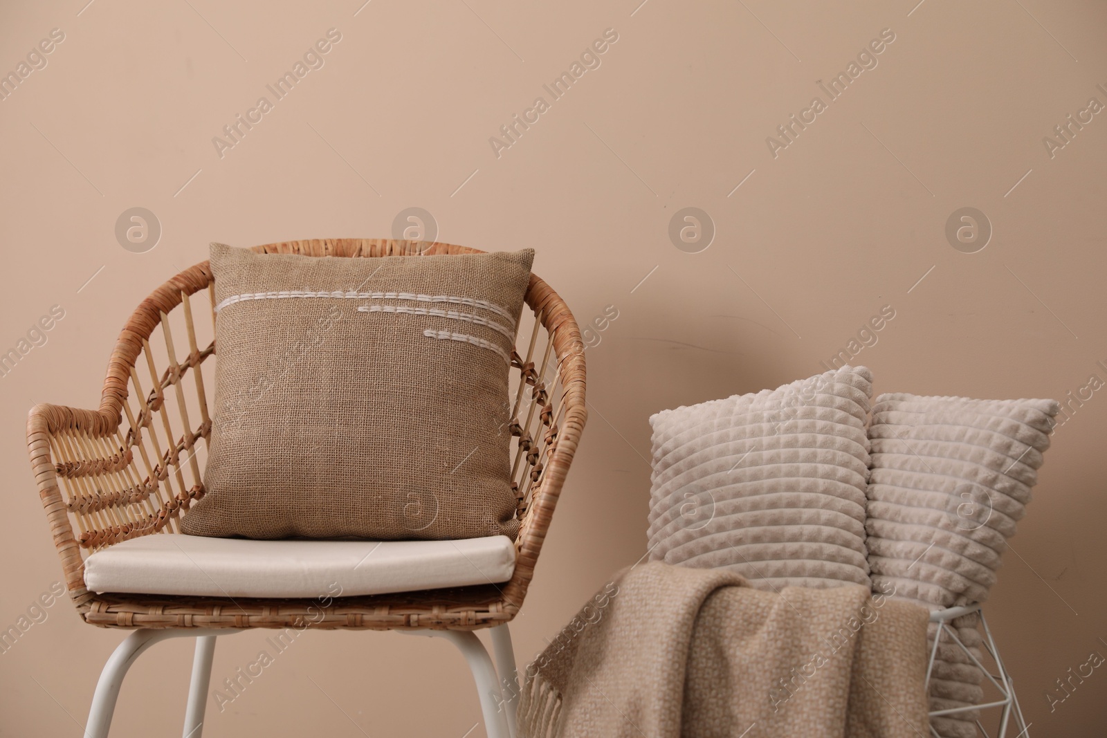 Photo of Soft pillows, wicker chair and blanket near beige wall