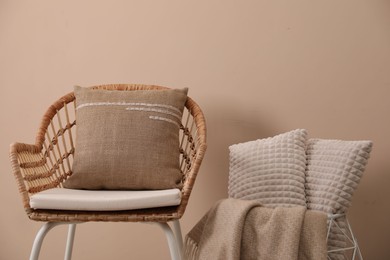 Soft pillows, wicker chair and blanket near beige wall