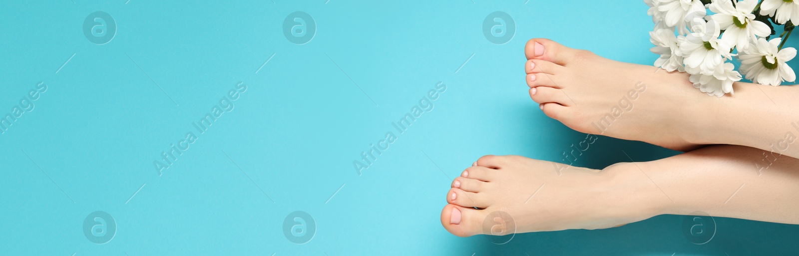 Image of Woman showing neat toenails after pedicure procedure and flowers on light blue background, top view. Banner design with space for text