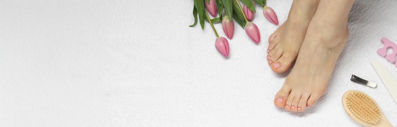 Image of Woman showing neat toenails after pedicure procedure and flowers on white towel, top view. Banner design with space for text