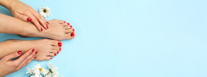 Image of Woman showing neat toenails and fingernails after pedicure and manicure procedures and flowers on light blue background, top view. Banner design with space for text