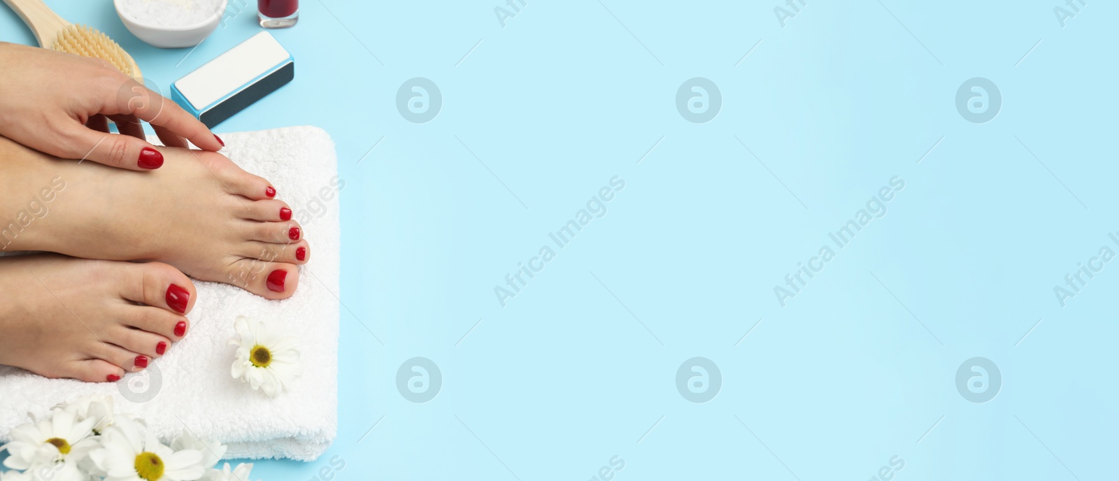 Image of Woman showing neat toenails and fingernails after pedicure and manicure procedures and flowers on light blue background, top view. Banner design with space for text