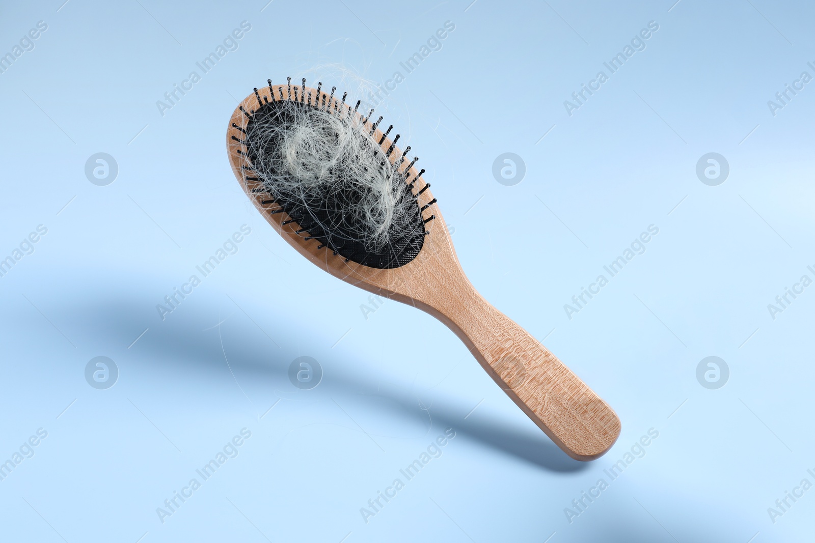 Photo of Wooden brush with lost hair in air on light blue background