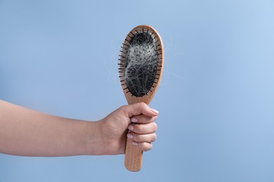 Photo of Woman holding brush with lost hair on light blue background, closeup. Space for text