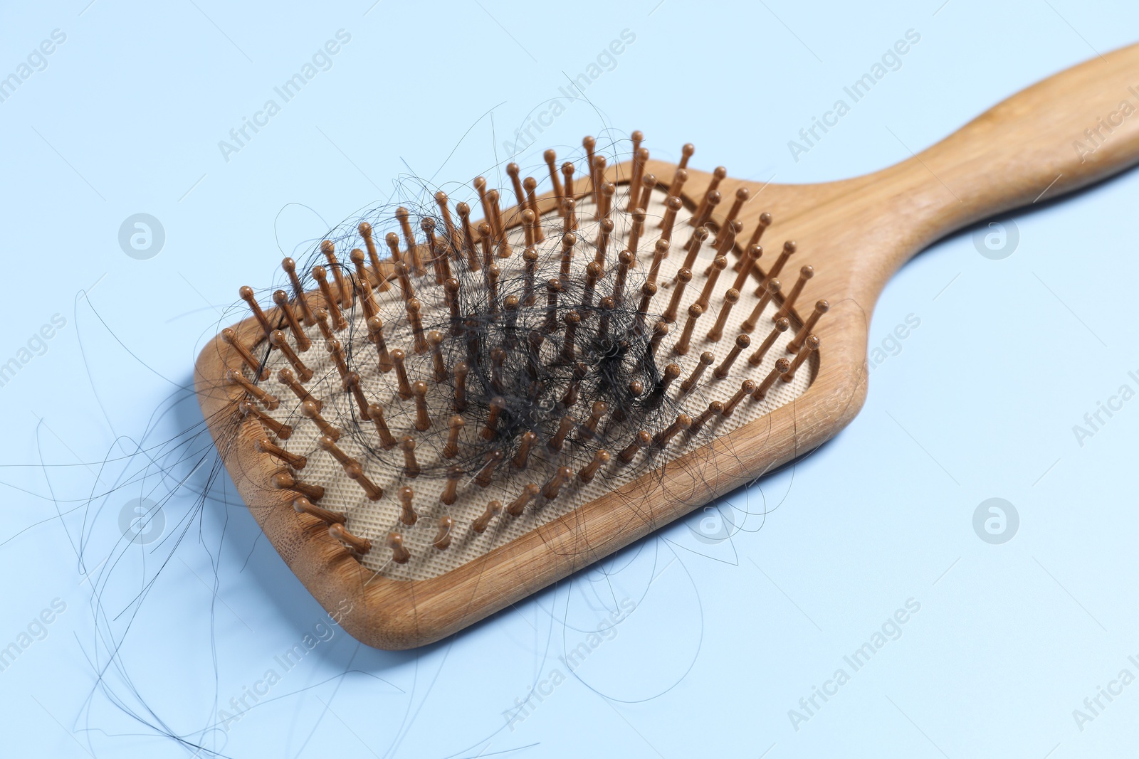 Photo of Wooden brush with lost hair on light blue background