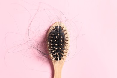 Photo of Wooden brush with lost hair on pink background, top view