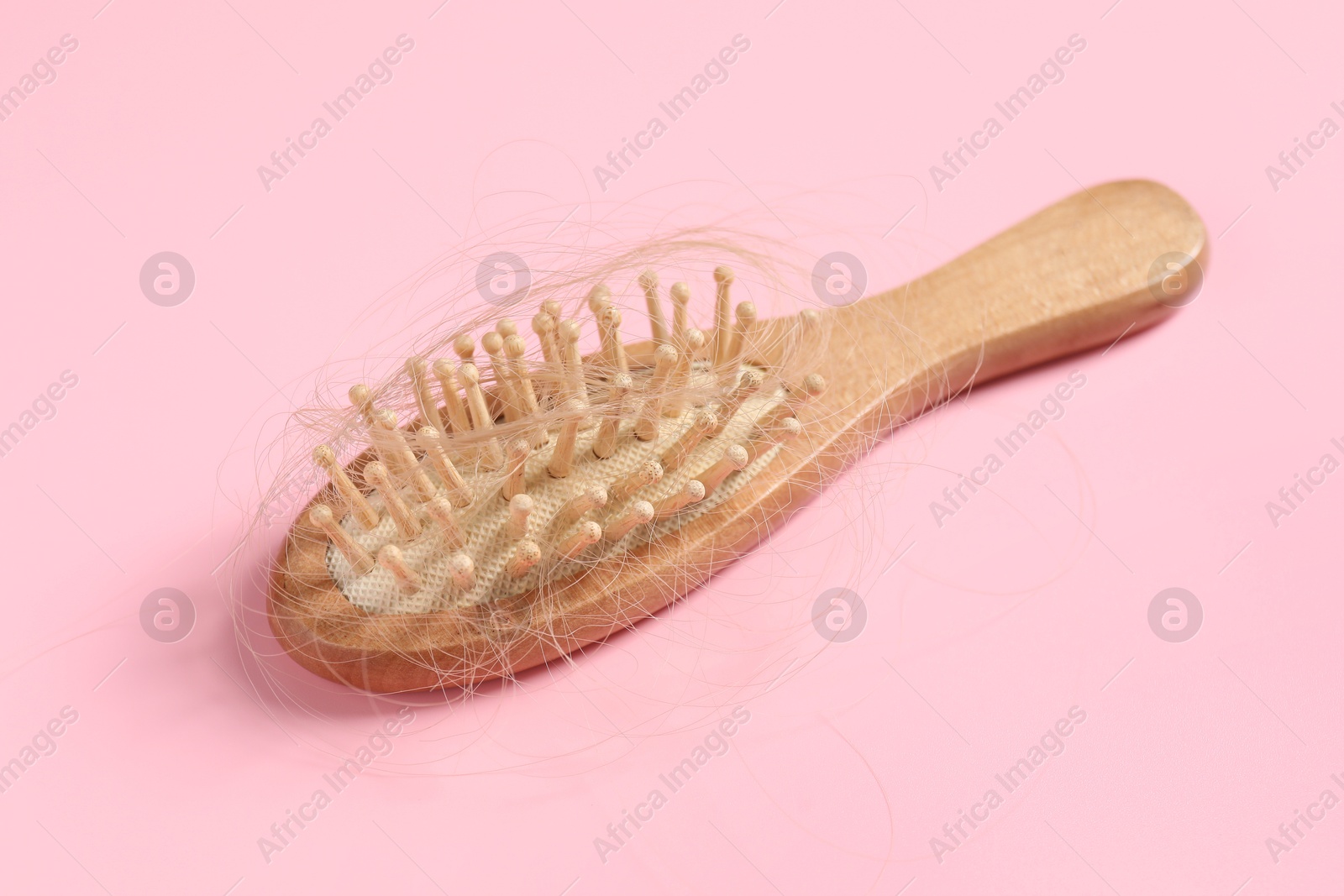 Photo of Wooden brush with lost hair on pink background