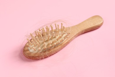 Photo of Wooden brush with lost hair on pink background