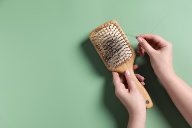 Woman holding brush with lost hair on green background, top view