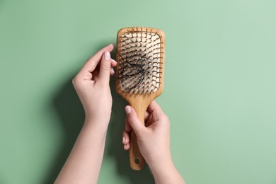 Photo of Woman holding brush with lost hair on green background, top view