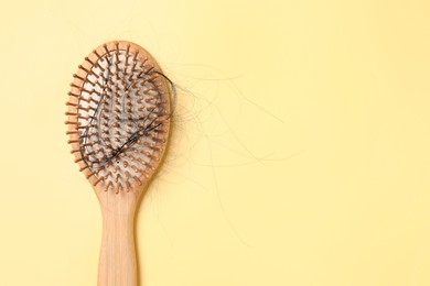 Photo of Wooden brush with lost hair on yellow background, top view. Space for text