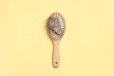 Photo of Wooden brush with lost hair on yellow background, top view