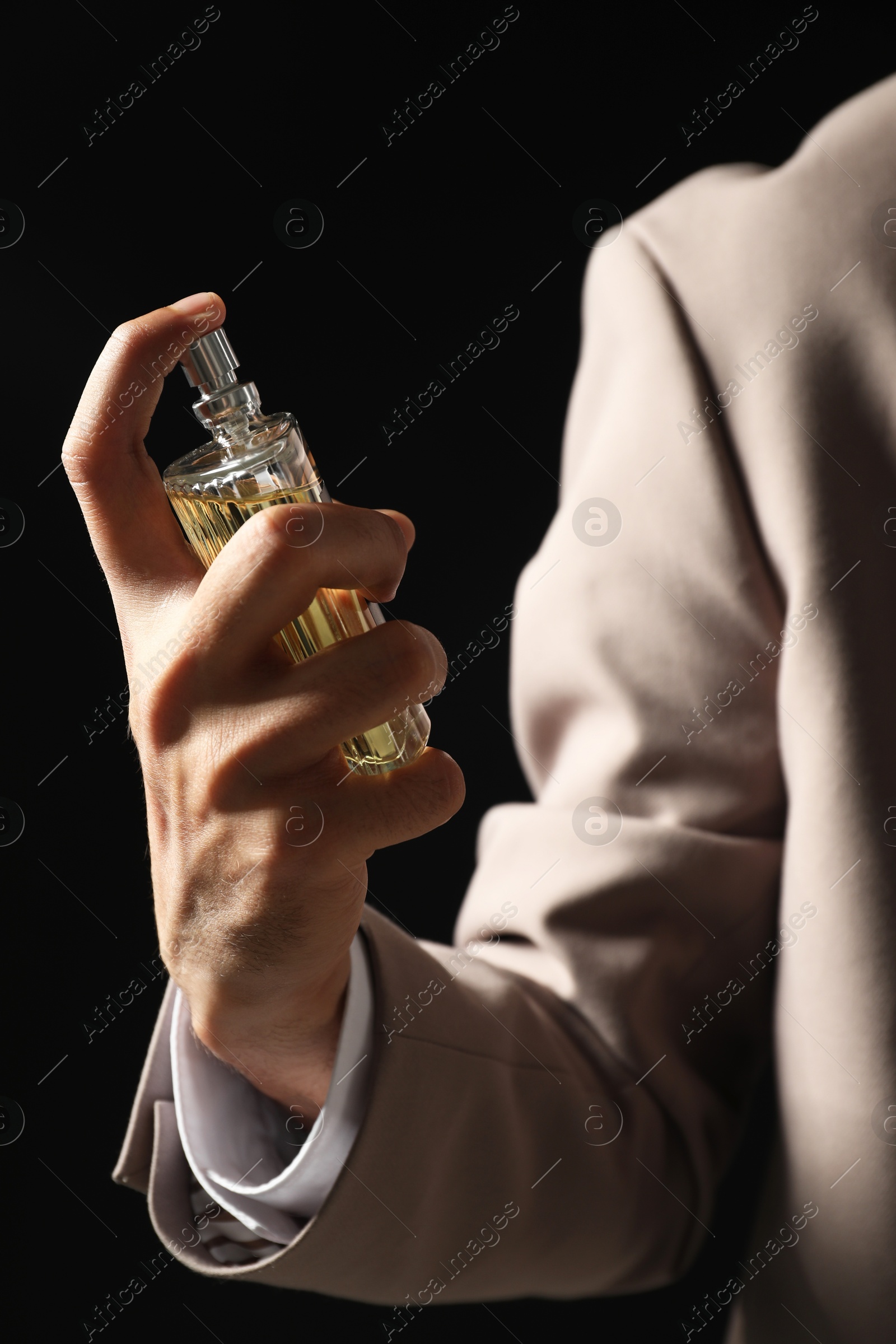 Photo of Man spraying luxury perfume on dark background, closeup