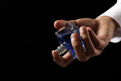 Photo of Man spraying luxury perfume on dark background, closeup. Space for text