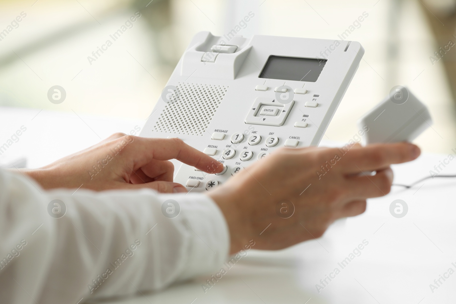 Photo of Assistant dialing number on telephone against blurred background, closeup