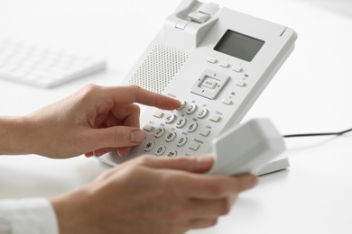 Assistant dialing number on telephone against blurred background, closeup