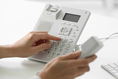Assistant dialing number on telephone against blurred background, closeup