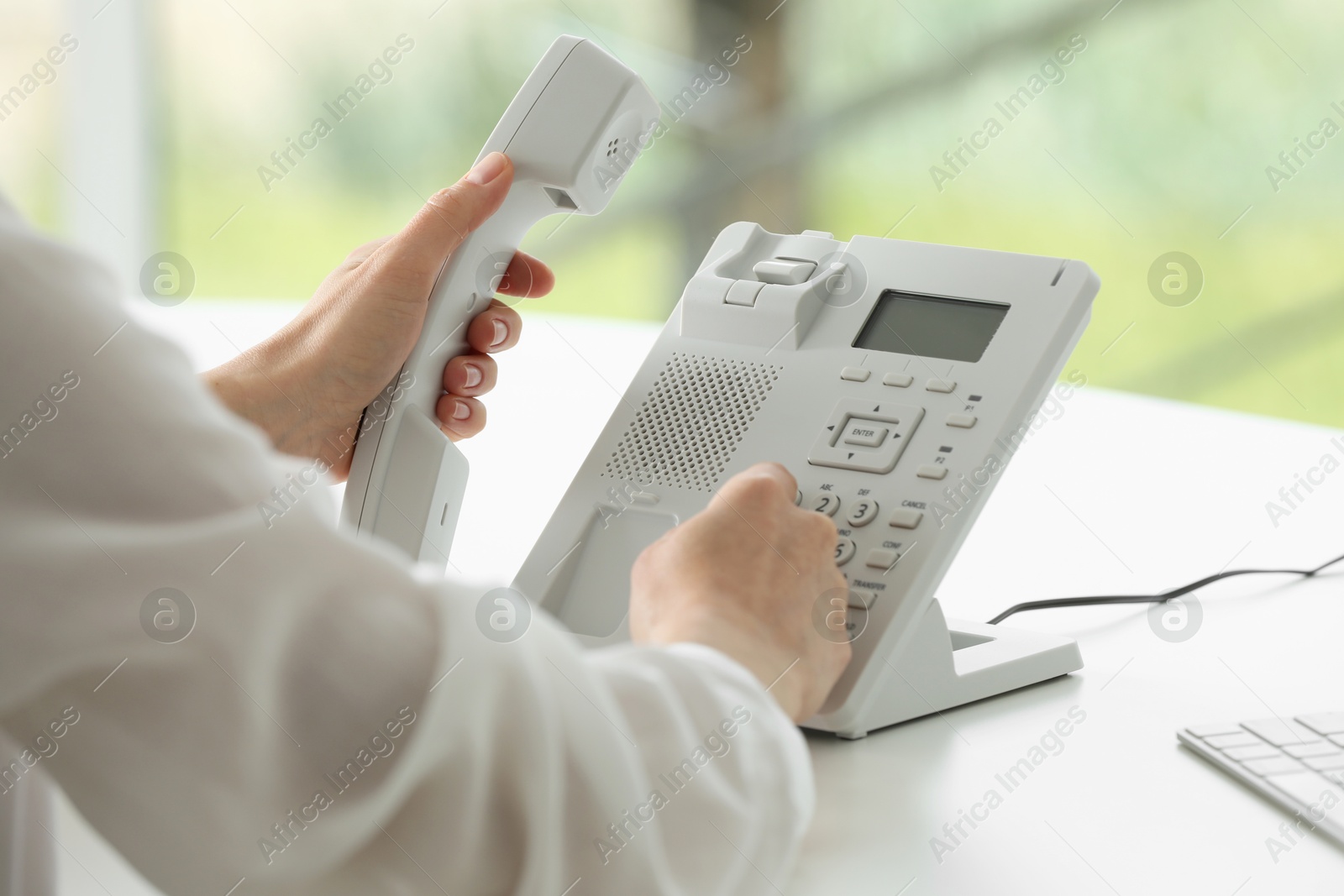 Photo of Assistant dialing number on telephone against blurred background, closeup