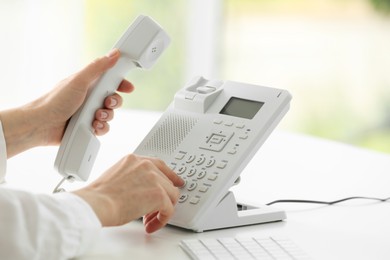 Photo of Assistant dialing number on telephone against blurred background, closeup