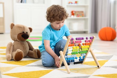 Cute little boy playing with wooden abacus on floor in kindergarten