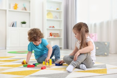 Cute little children playing with set of wooden geometric figures on floor in kindergarten