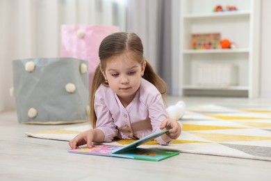 Cute little girl reading book on floor in kindergarten