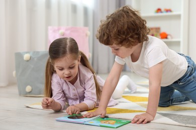 Cute little children reading book on floor in kindergarten