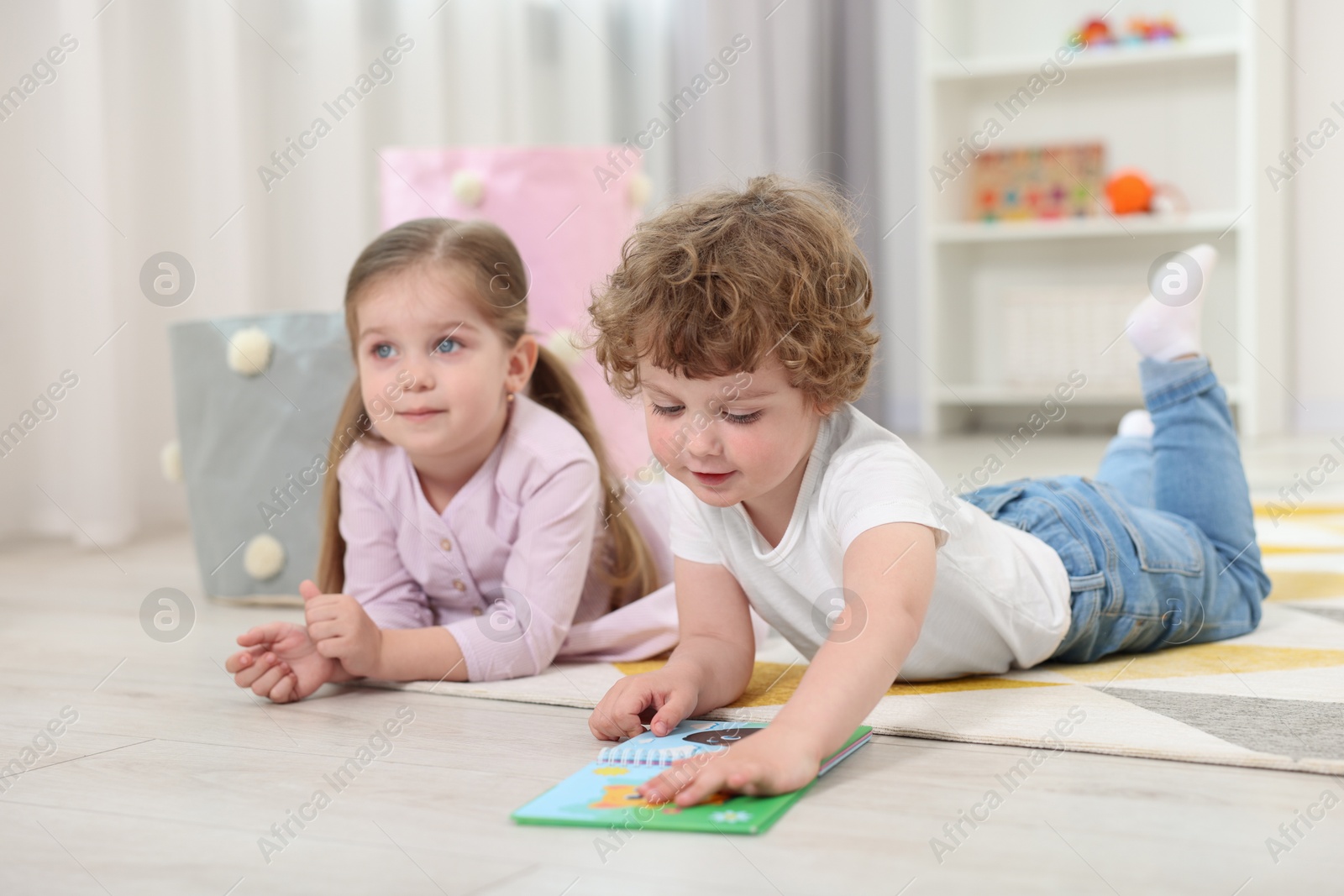 Photo of Cute little children reading book on floor in kindergarten